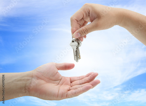 hand giving set of house keys against blue sky and sun