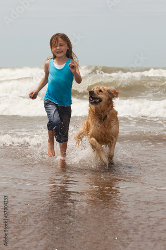 child and her dog playing by the ocean