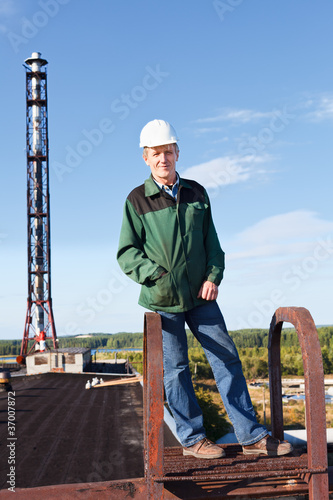 Worker in white hardhat in roof against industrial chimney