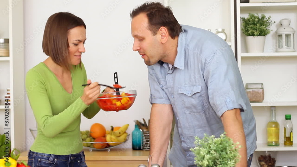 Young happy couple preparing and tasting salad in the kitchen Young happy couple preparing and tasting salad in the kitchen