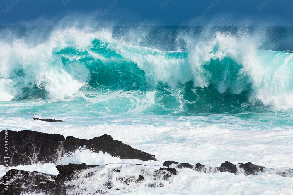 Fototapeta Turquoise rolling wave slaming on the rocks