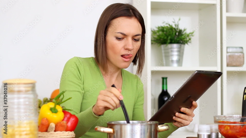 Woman cooking, tasting and looking at recipe on digital tablet Woman cooking, tasting and looking at recipe on digital tablet