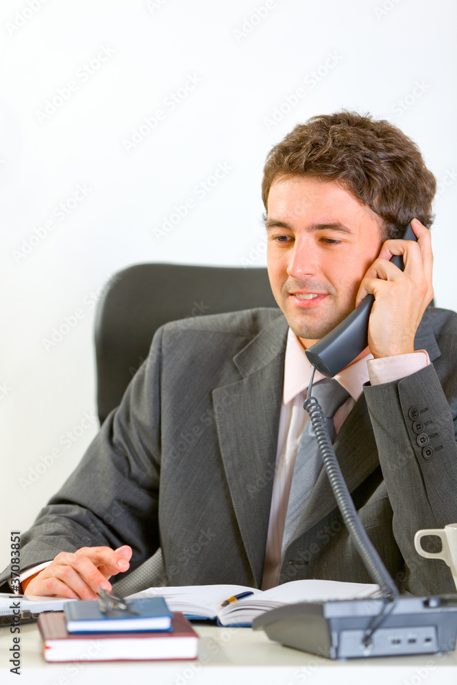 Modern businessman sitting at office and speaking phone Modern businessman sitting at office and speaking phone