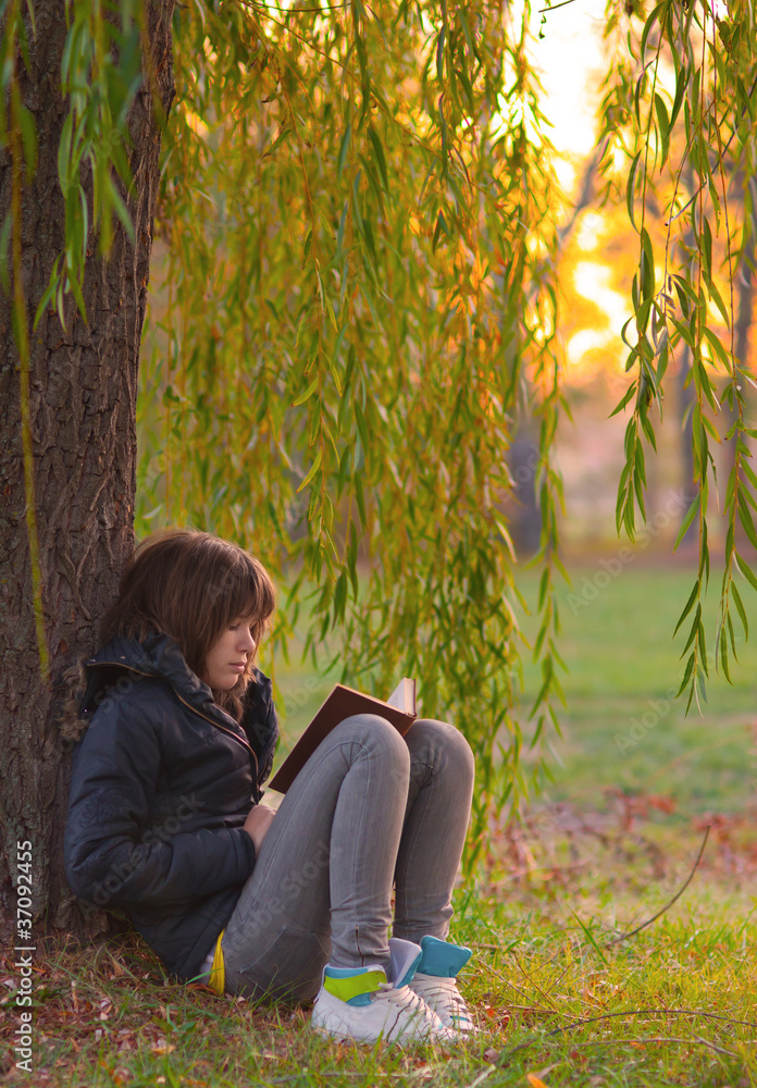 Pretty teenage girl reads the book under the willow tree