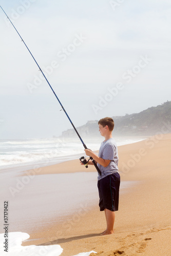 young teenage boy fishing on beach alone