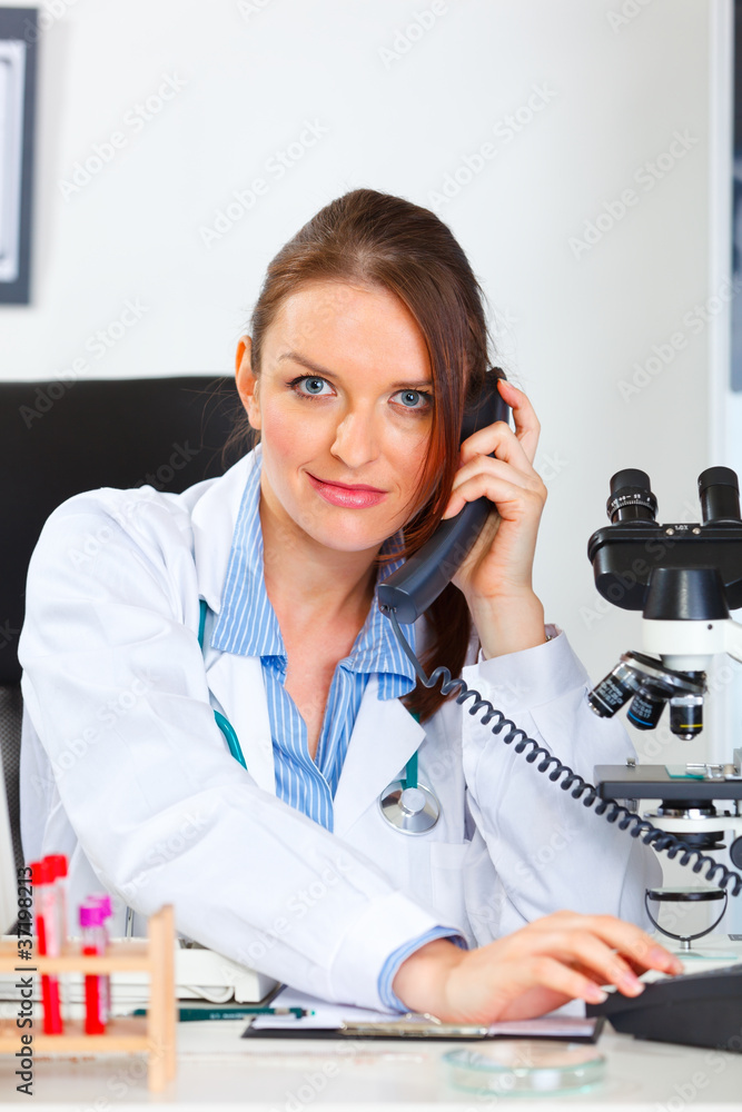 Female medical doctor sitting in cabinet and making phone call Female medical doctor sitting in cabinet and making phone call