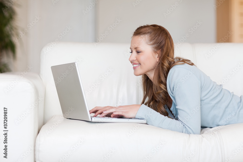 Cheerful smiling woman on the sofa typing on her laptop Cheerful smiling woman on the sofa typing on her laptop