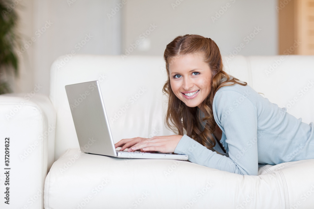 Cheerful smiling woman on the couch typing on her laptop Cheerful smiling woman on the couch typing on her laptop