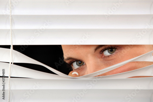 Фотография Woman peeking through venetian blinds