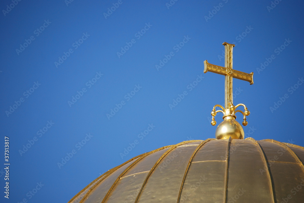 Golden orthodox cross and dome close-up on blue-sky background