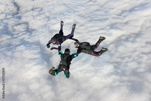 Three skydivers in freefall over a bank of clouds