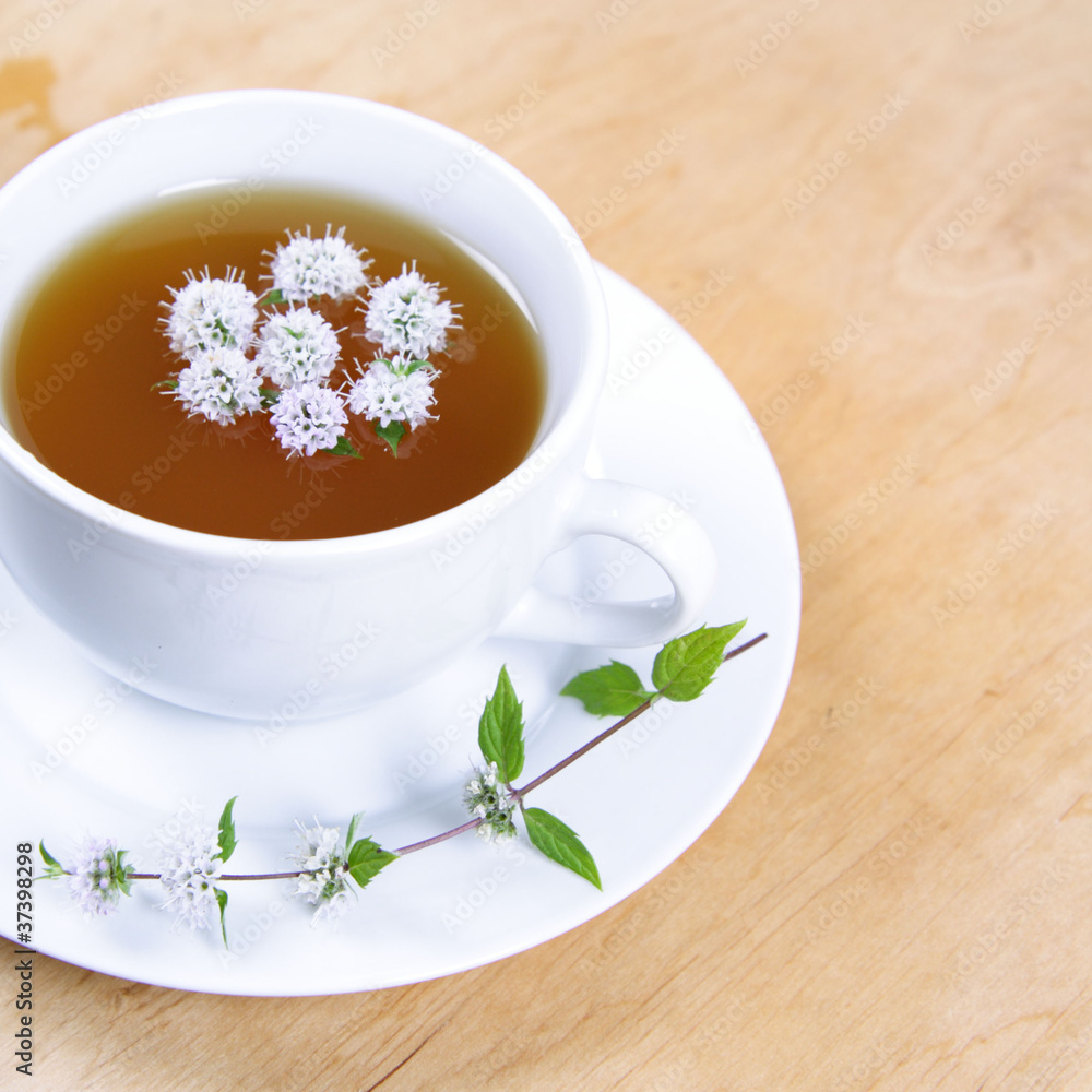 Cup of green tea with flowers of peppermint floating in it Cup of green tea with flowers of peppermint floating in it
