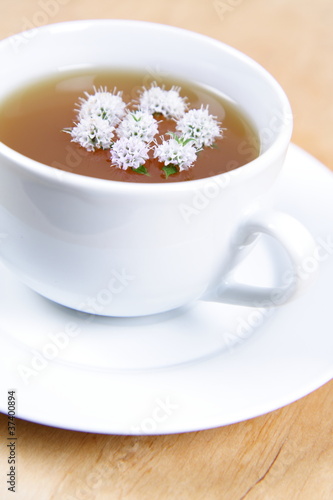 Cup of green tea with flowers of peppermint floating in it