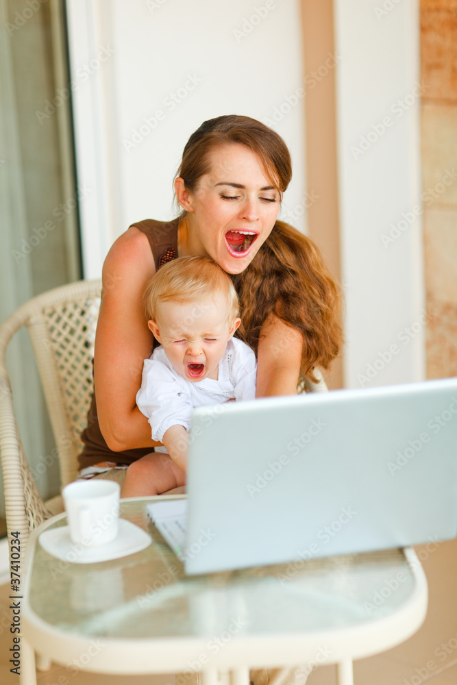 Young mother and baby yawing while working on laptop Young mother and baby yawing while working on laptop