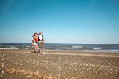 couple with backpacks walking on sea shore