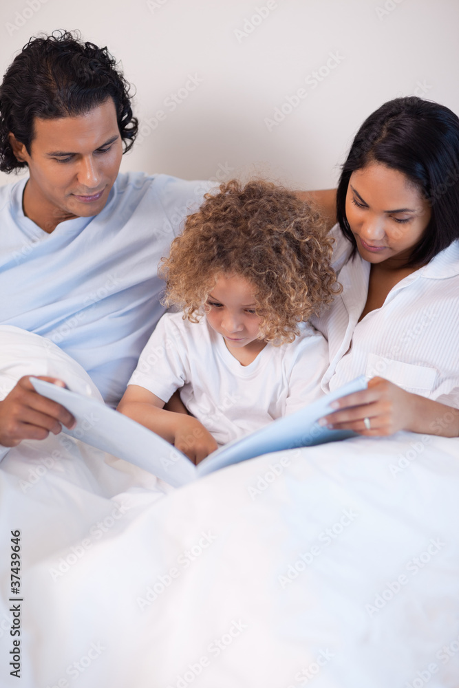 Family sitting on the bed reading a story Family sitting on the bed reading a story