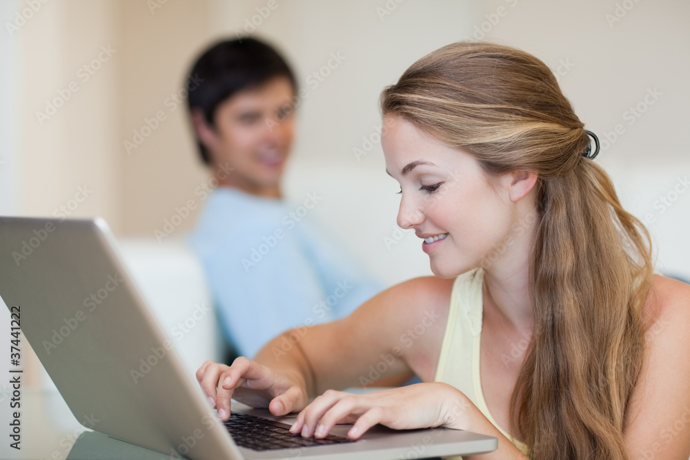Woman using a laptop while her husband is sitting on a sofa