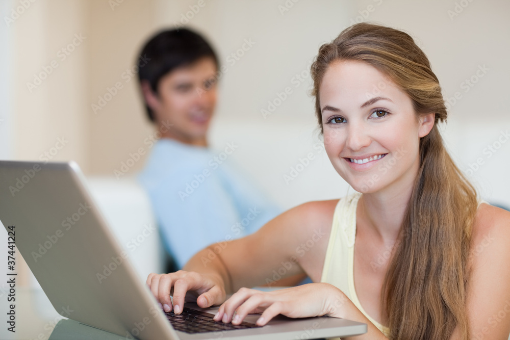 Woman using a laptop while her husband is sitting on a couch Woman using a laptop while her husband is sitting on a couch