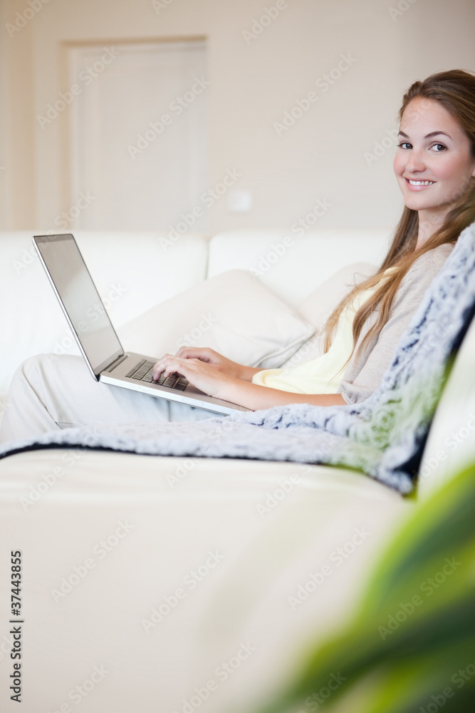 Side view of smiling woman with her laptop sitting on the sofa Side view of smiling woman with her laptop sitting on the sofa