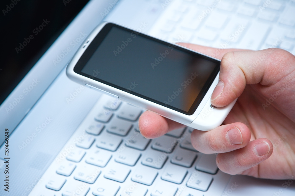 smart phone in hand with laptop keyboard backgroun smart phone in hand with laptop keyboard backgroun