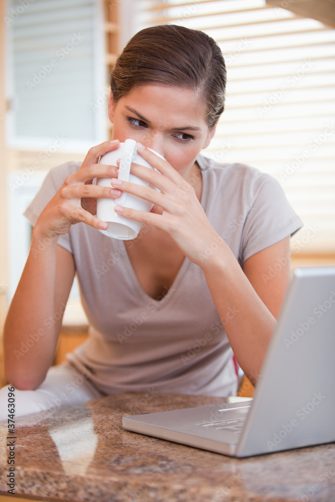 Woman taking a sip of coffee next to her laptop Woman taking a sip of coffee next to her laptop