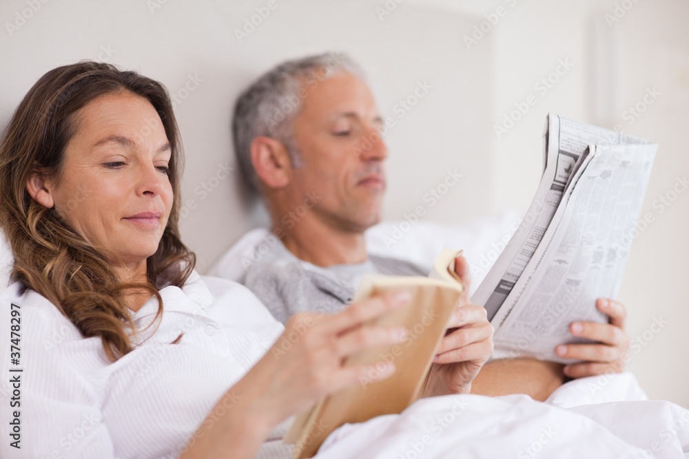Obraz premium Woman reading a book while her husband is reading the news