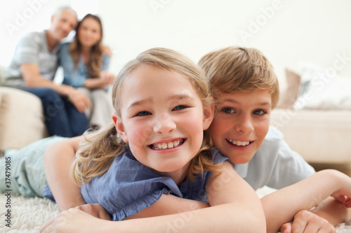 Happy siblings posing on a carpet with their parents on the back