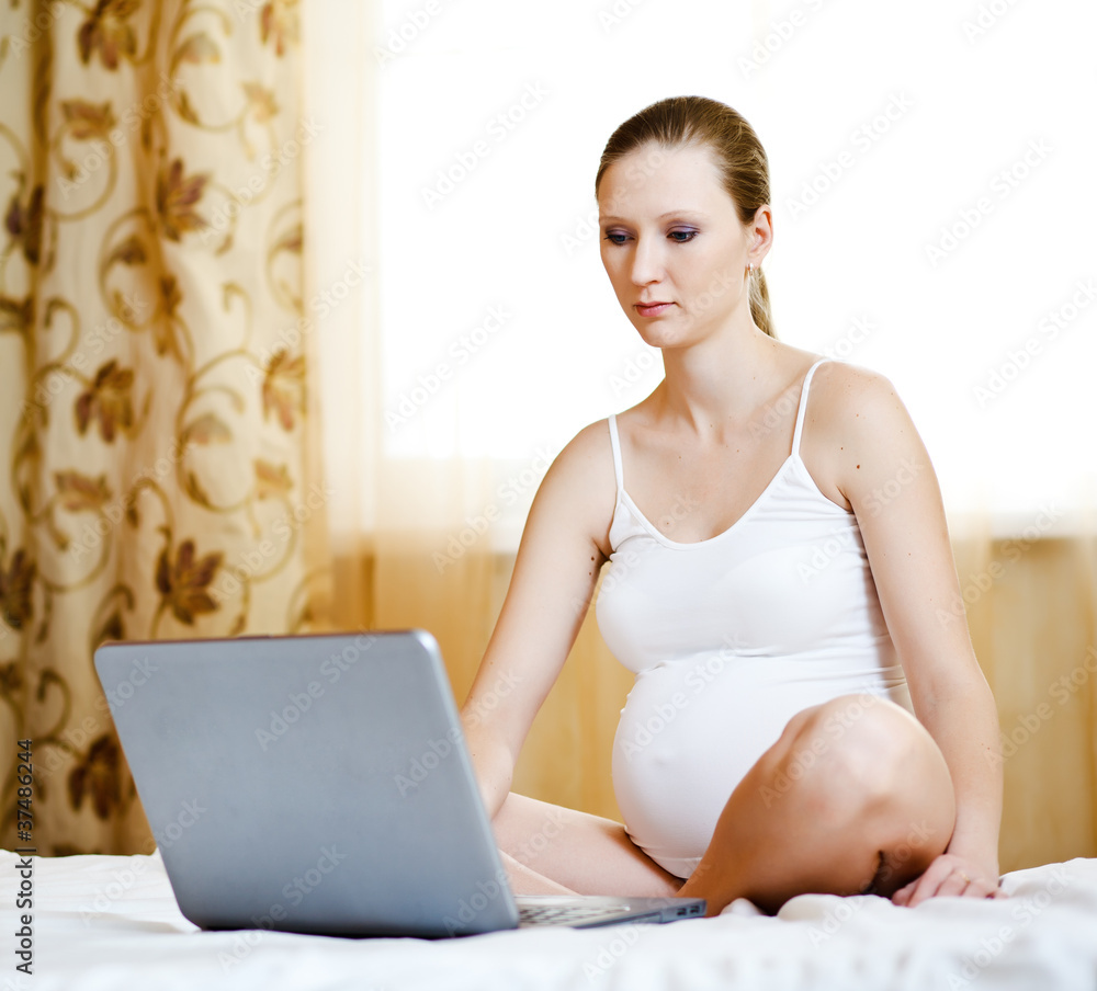 pregnant woman relaxing with her laptop on a bed at home pregnant woman relaxing with her laptop on a bed at home
