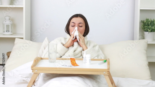 Sick young woman blowing nose and spraying medicine in nostril