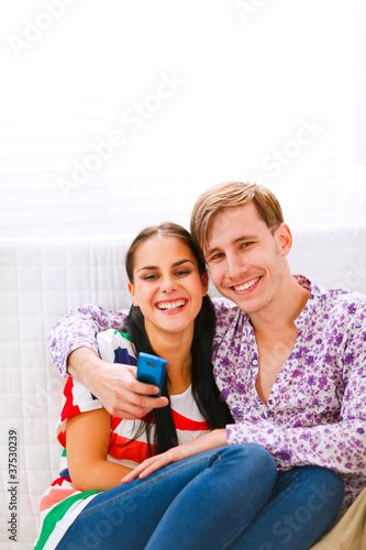 Young smiling couple sitting on couch with mobile
