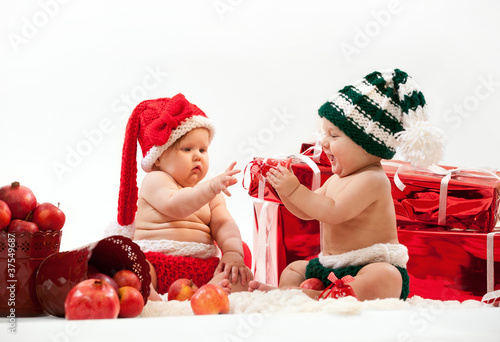 Two cute babies, in Christmas costumes playing among gifts photo