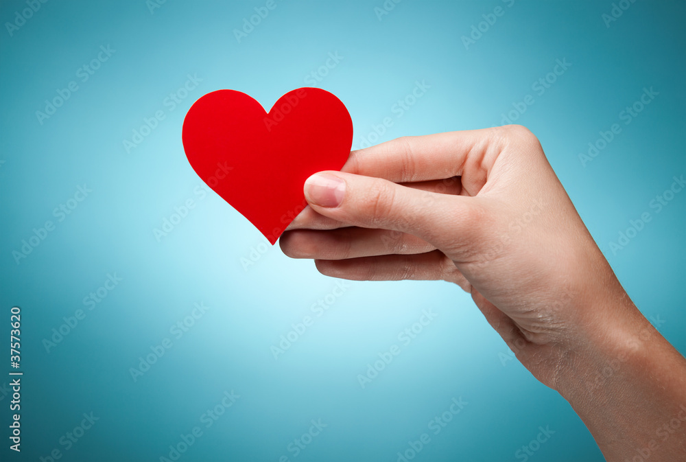 woman's hand holding symbol - red heart. Against blue background woman's hand holding symbol - red heart. Against blue background