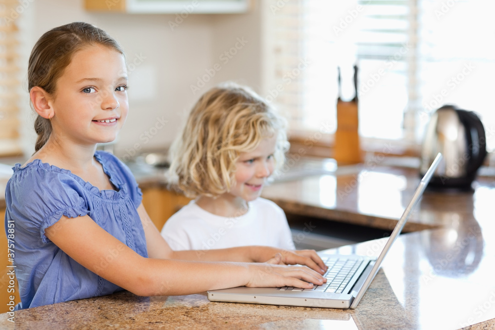 Siblings with laptop behind the kitchen counter Siblings with laptop behind the kitchen counter