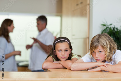 Sad looking siblings with fighting parents behind them