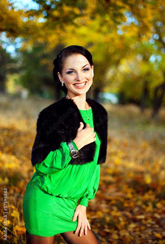 beautiful brunette in a green dress walks on autumn park