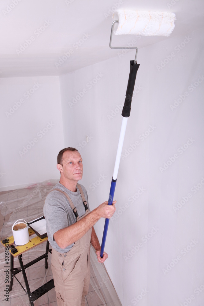 Decorator using a roller extension to paint a ceiling white Decorator using a roller extension to paint a ceiling white