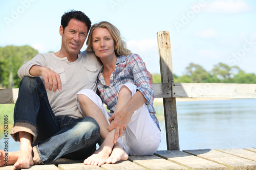 mid age couple seated on a pontoon near a lake
