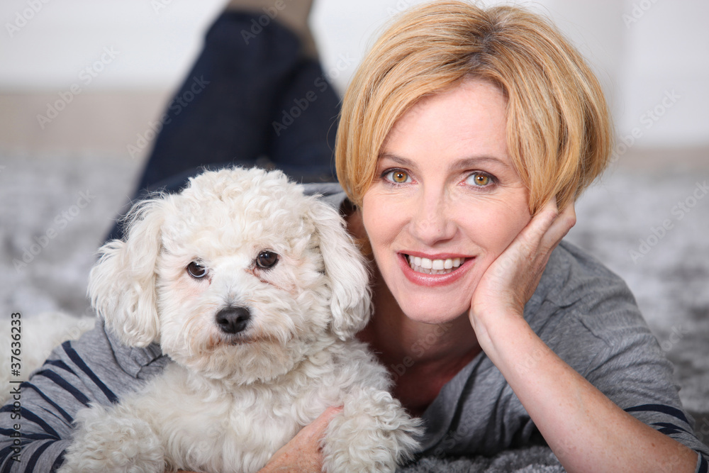 Blonde woman lying on the carpet with a small fluffy white dog Blonde woman lying on the carpet with a small fluffy white dog