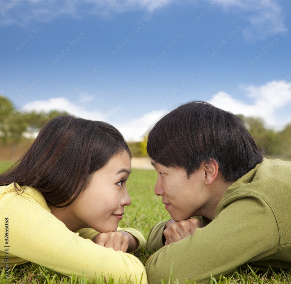 Happy asian couple lying on the grass with cloud background Happy asian couple lying on the grass with cloud background