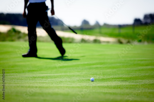 Legs of golfer watching ball roll near hole on green
