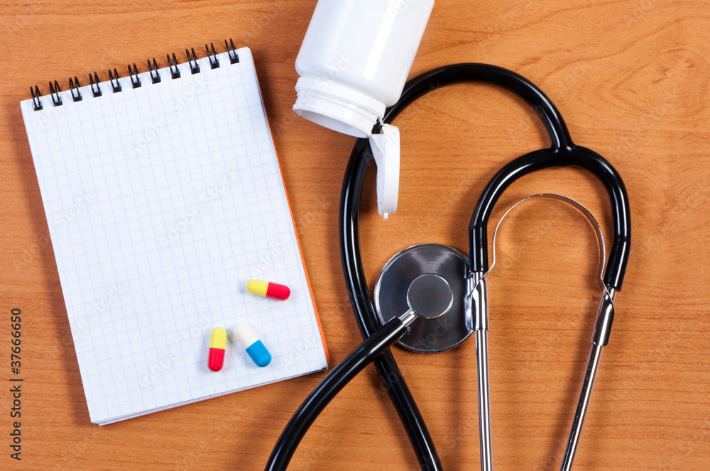 Fotografie Stethoscope, notepad and pills on table. View from above.