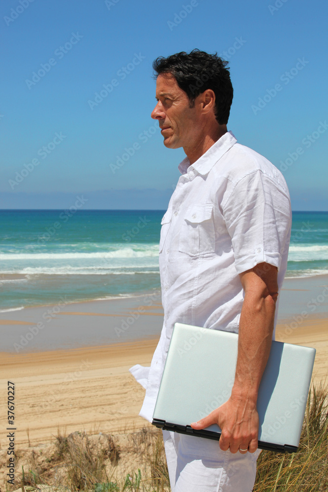 Man looking out to sea with laptop under arm.