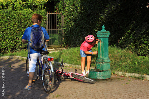 Bambina ciclista che beve alla fontana
