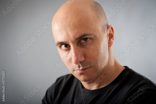 Bald man with proud expression. Grey background.