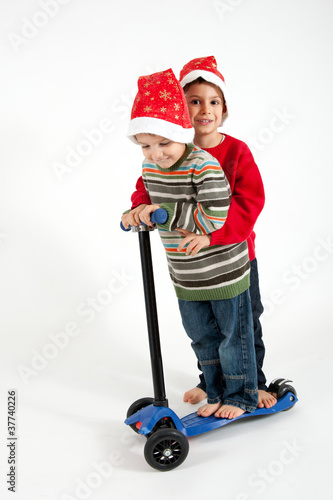 Two Brothers playing together with christmas hat and scooter on