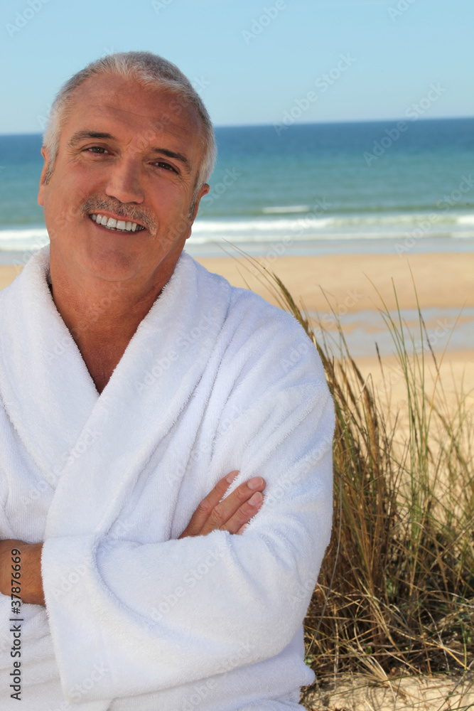 Grey haired man in bathing robe stood on beach