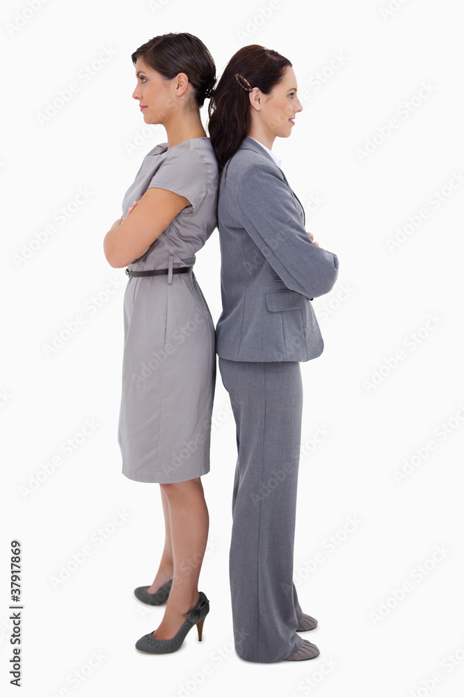 Businesswomen with arms folded standing back on back Businesswomen with arms folded standing back on back