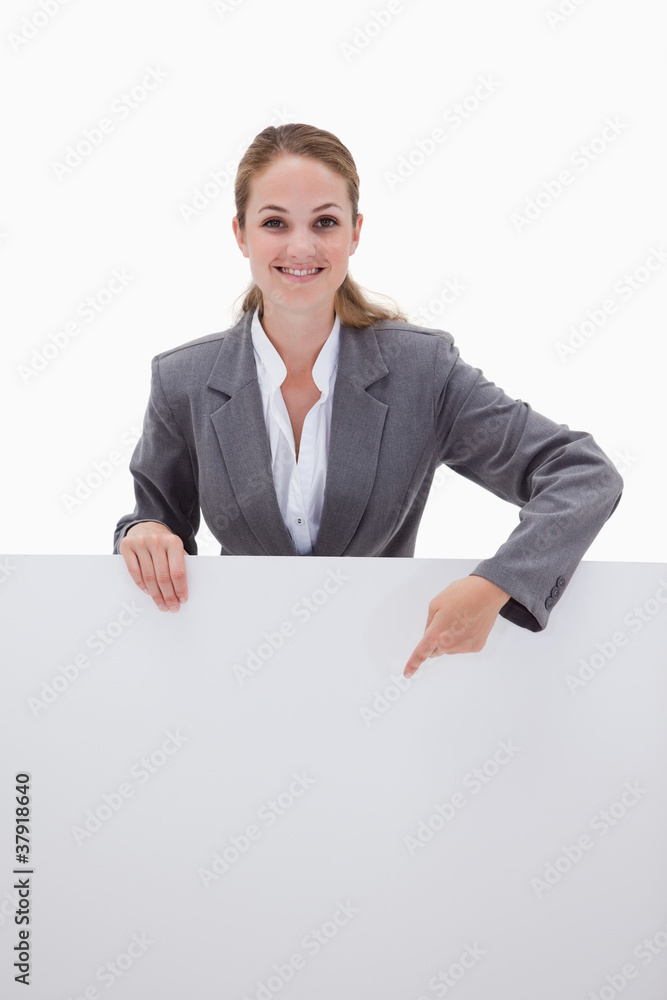 Smiling bank employee pointing down at blank sign Smiling bank employee pointing down at blank sign