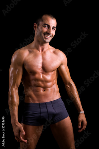 Smiling muscular young man posing against black background