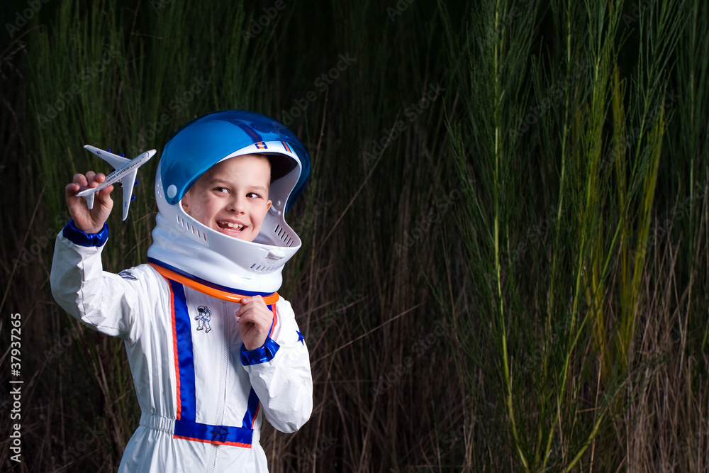 Happy boy dressed as astronaut playing with toy plane